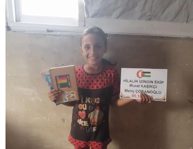 Kırtasiye yardımı olarak aldığı defter ve kalemleri tutan gülümseyen bir kız çocuğu