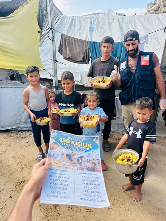 Gönüllüyle birlikte yemek kaplarını tutan çocuklar